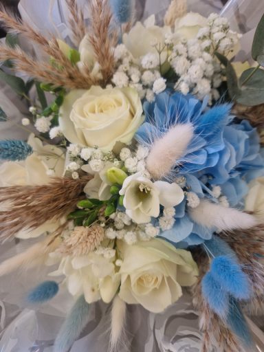 A bouquet featuring white roses, blue hydrangea, white freesia, gypsophila and decorative grasses