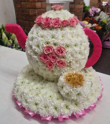 Teapot and teacup arrangement made of white flowers, decorated with pink rosebuds and ribbon.