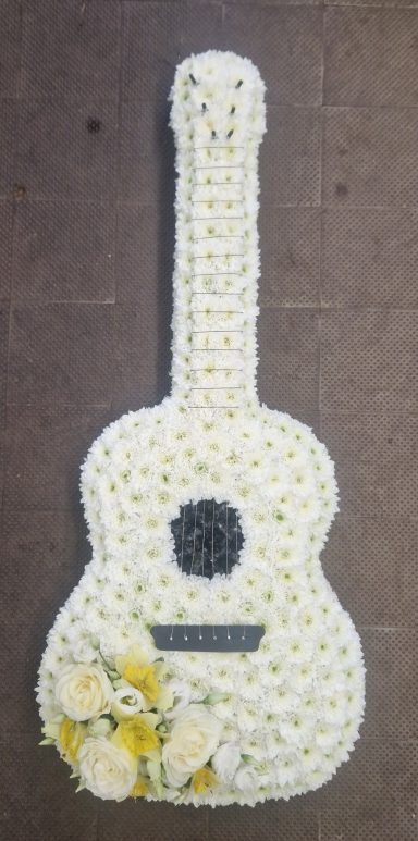 Floral guitar tribute, adorned with white and yellow flowers.