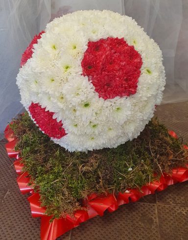 A floral football tribute with red and white flowers on a mossy base.